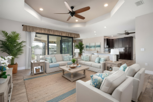 Living room with beige sofas, white armchairs, wooden coffee table, large rug, plants, and open kitchen.