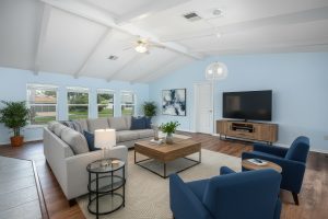 Living room with light blue walls, vaulted ceiling, beige sectional, blue chairs, and wooden furniture.