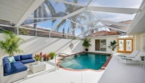 Screened-in pool area with blue cushioned wicker sofa, lounge chairs, and tropical plants.