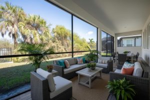 Screened patio with wicker seating, cushions, coffee table, potted plants, and dining area.