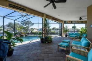 Screened outdoor patio with wicker furniture, blue cushions, potted plants, and swimming pool.