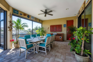 Outdoor dining area with white chairs, teal cushions, potted plants, and glass windows.