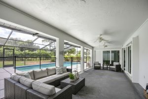 Covered patio with sectional sofa, armchairs, coffee table, ceiling fans, and pool view.