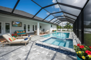 Covered outdoor pool area with pool, hot tub, lounge chairs, seating, and mounted TV.