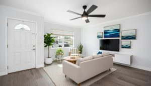 Living room with beige sofa, round wooden table, wall-mounted TV, blue artwork, and plants.