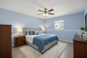 Bedroom with light blue walls, large bed with blue bedding, wooden furniture, ceiling fan, and window.