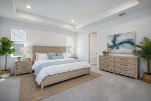 Modern bedroom with wooden bed, two nightstands, dresser, plants, abstract painting, and recessed lighting.