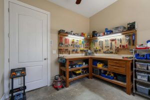 Corner workshop with wooden benches, pegboard tools, storage bins, and a vacuum cleaner.