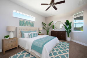 Bedroom with white and teal bedding, wooden nightstands, dark dresser, round mirror, ceiling fan, and large plants.