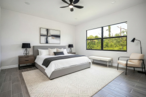 Modern bedroom with large bed, nightstands, lamps, armchair, bench, large window, and ceiling fan.