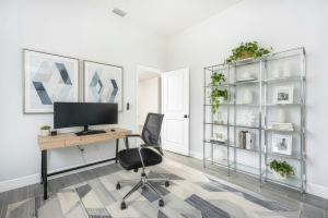 Home office with wooden desk, widescreen monitor, black office chair, metal shelves, and geometric rug.