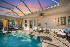 Indoor pool area with tiled floor, cushioned seating, ceiling fan, turquoise decor, and screened roof.